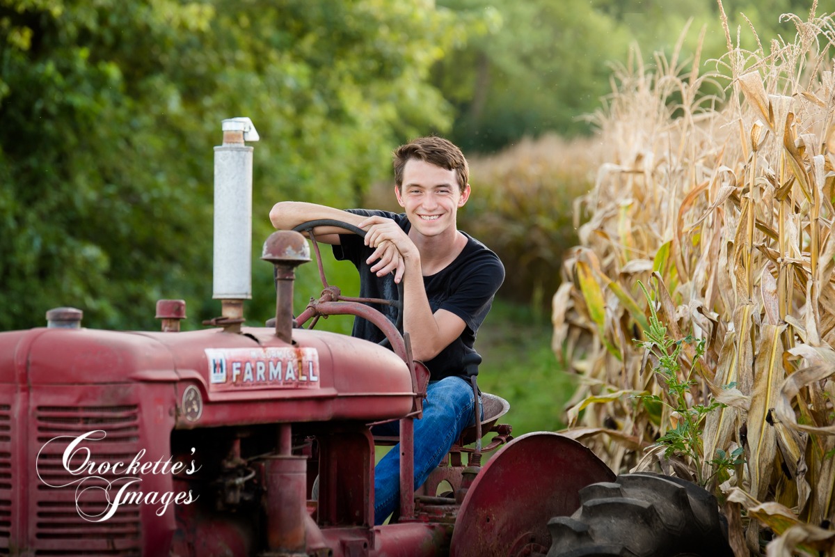 Fall Senior Boy photo sitting on a tractor next to a corn field.
