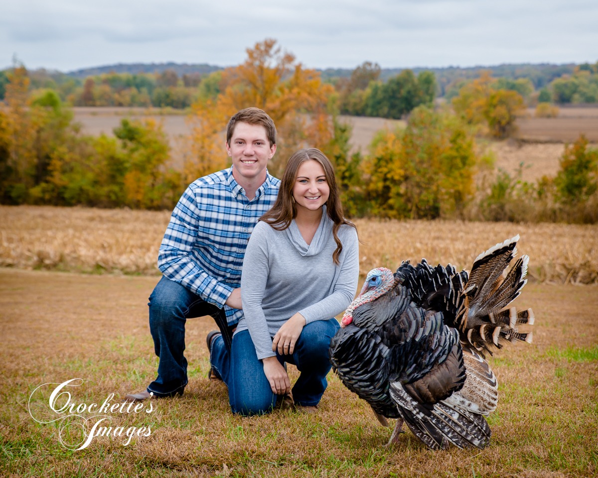 Fall engagement photo in a cut corn field with a wild tom turkey