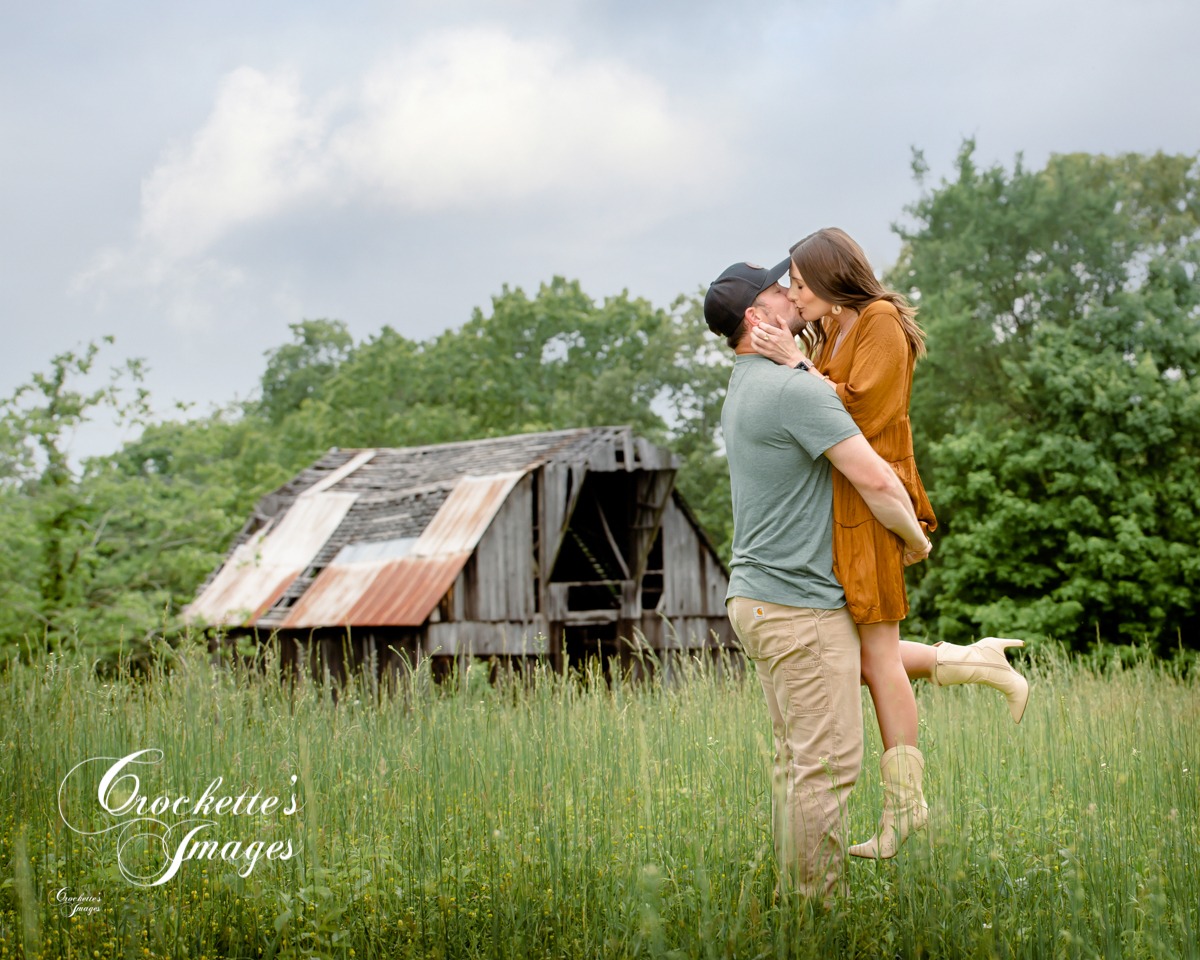 Farm engagement photo with couple kissing in a field with bard in the background