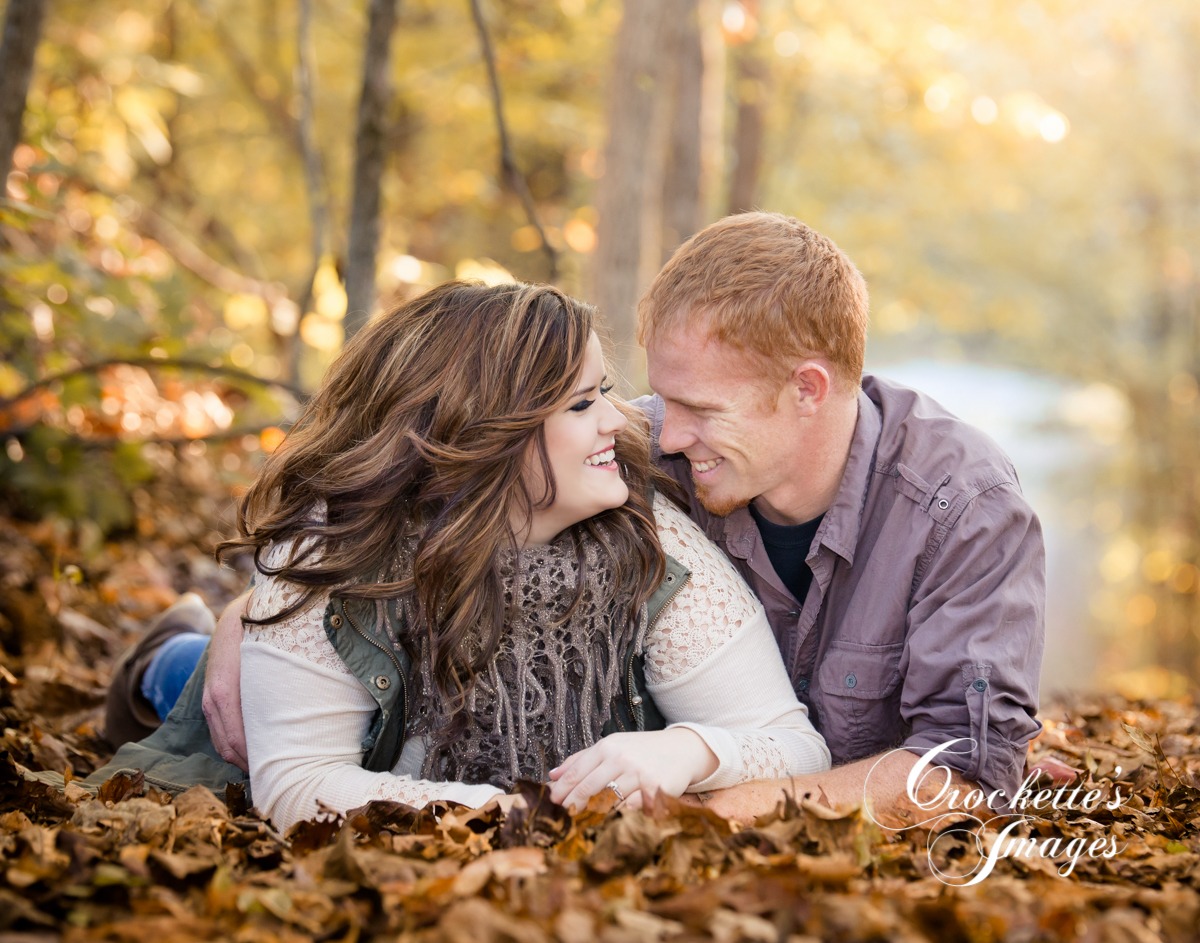 fun fall engagement photo with couple laying in fall leaves laughing