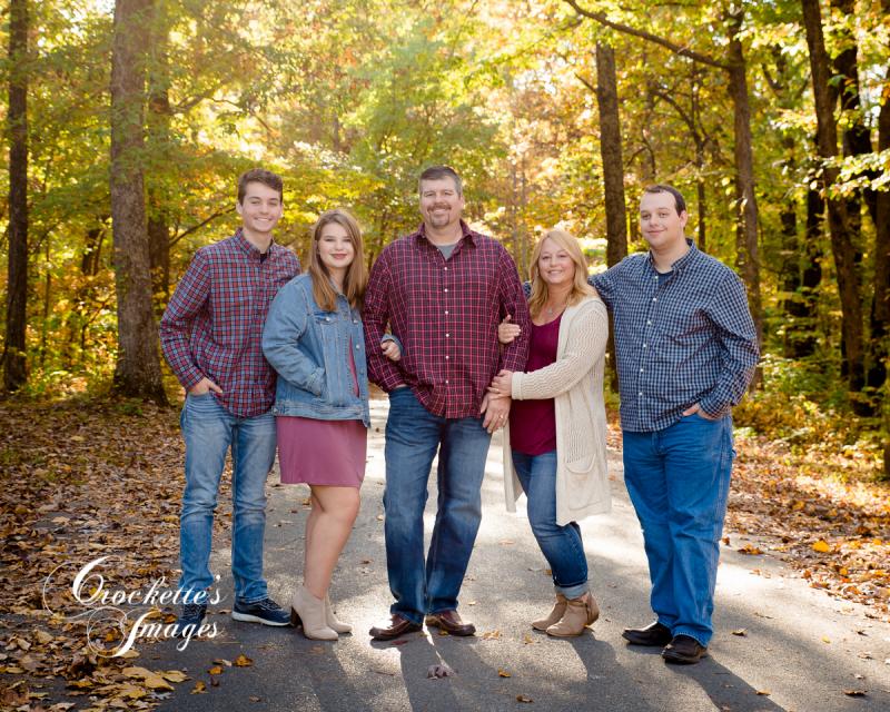 Fall Family Photo on road surrounded by trees. Blue, Maroon, and cream clothing color scheme.