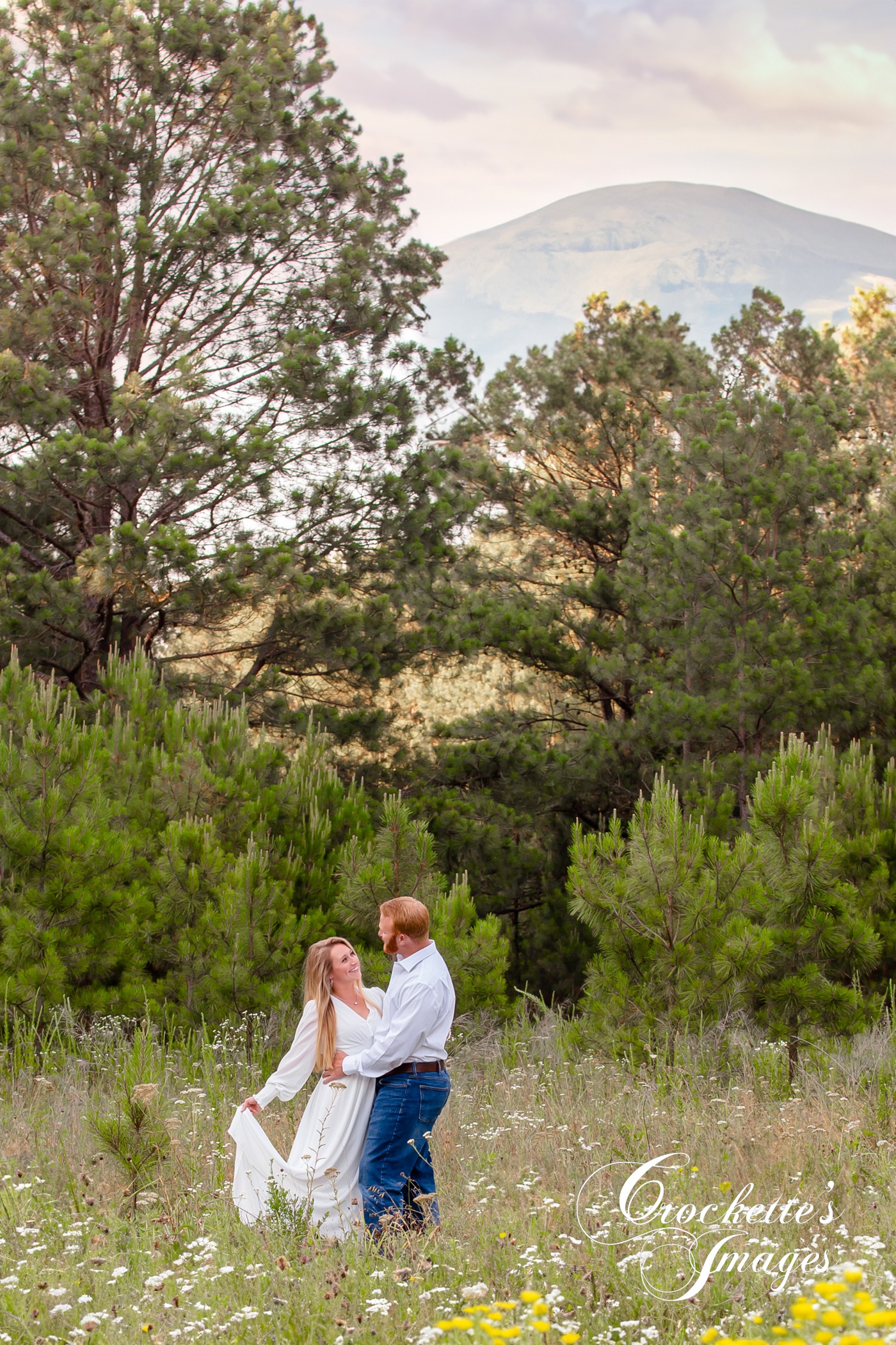 Dreamy Engagement Photos in a flower field surrounded by pine trees. White clothing color scheme