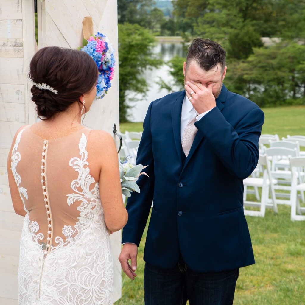 Groom wiping away tears during an emotional first look as he sees his bride for the first time outdoors before the wedding ceremony.