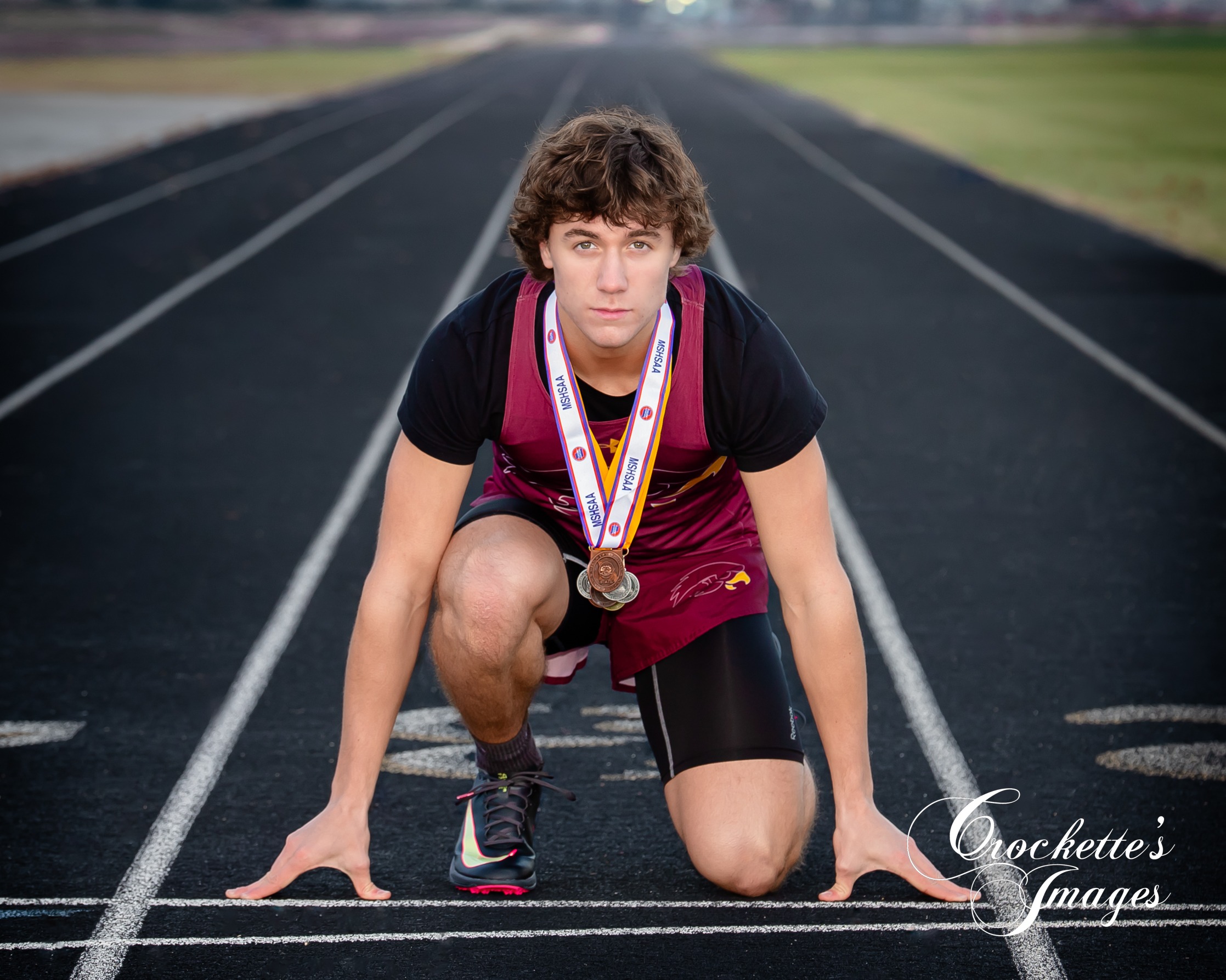 Powerful and tough senior photo of a boy on a high school track wearing his medals