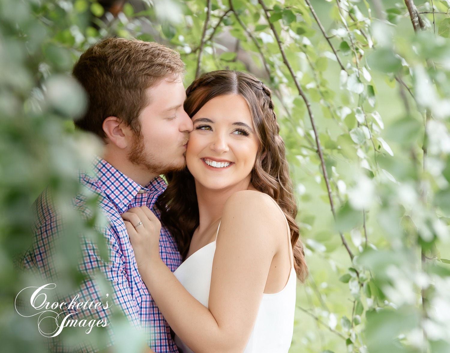 Romantic engagement photo with couple kissing in the trees