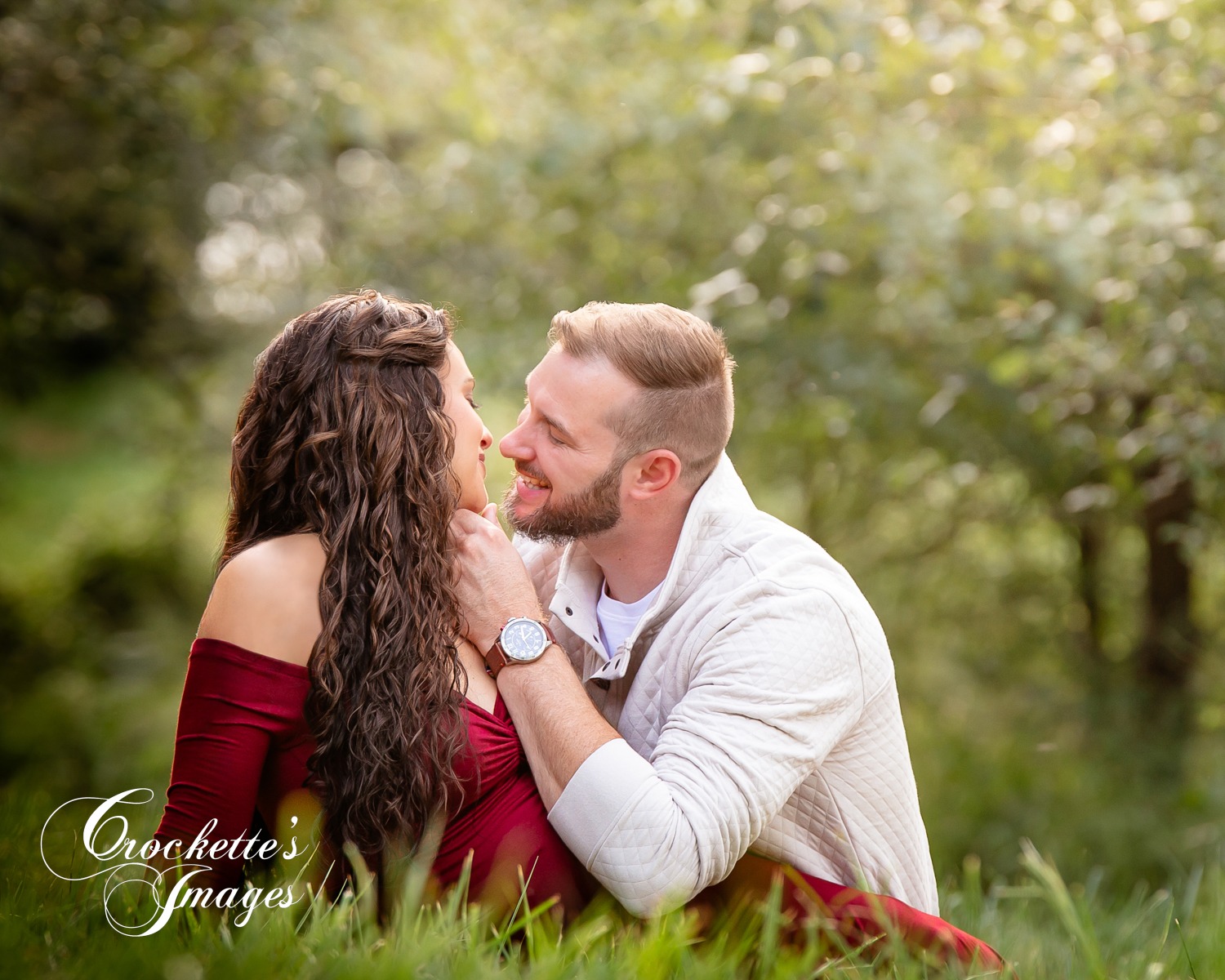 Engagement photo in the trees sitting in the grass laughing together