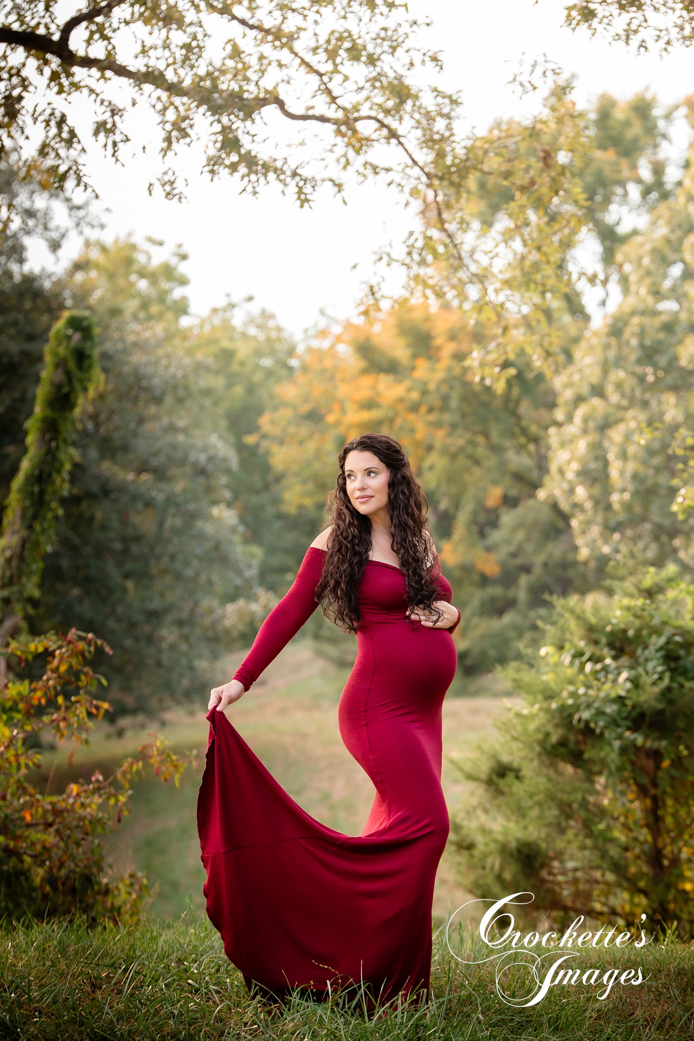 Stunning maternity photo in the trees wearing a maroon dress