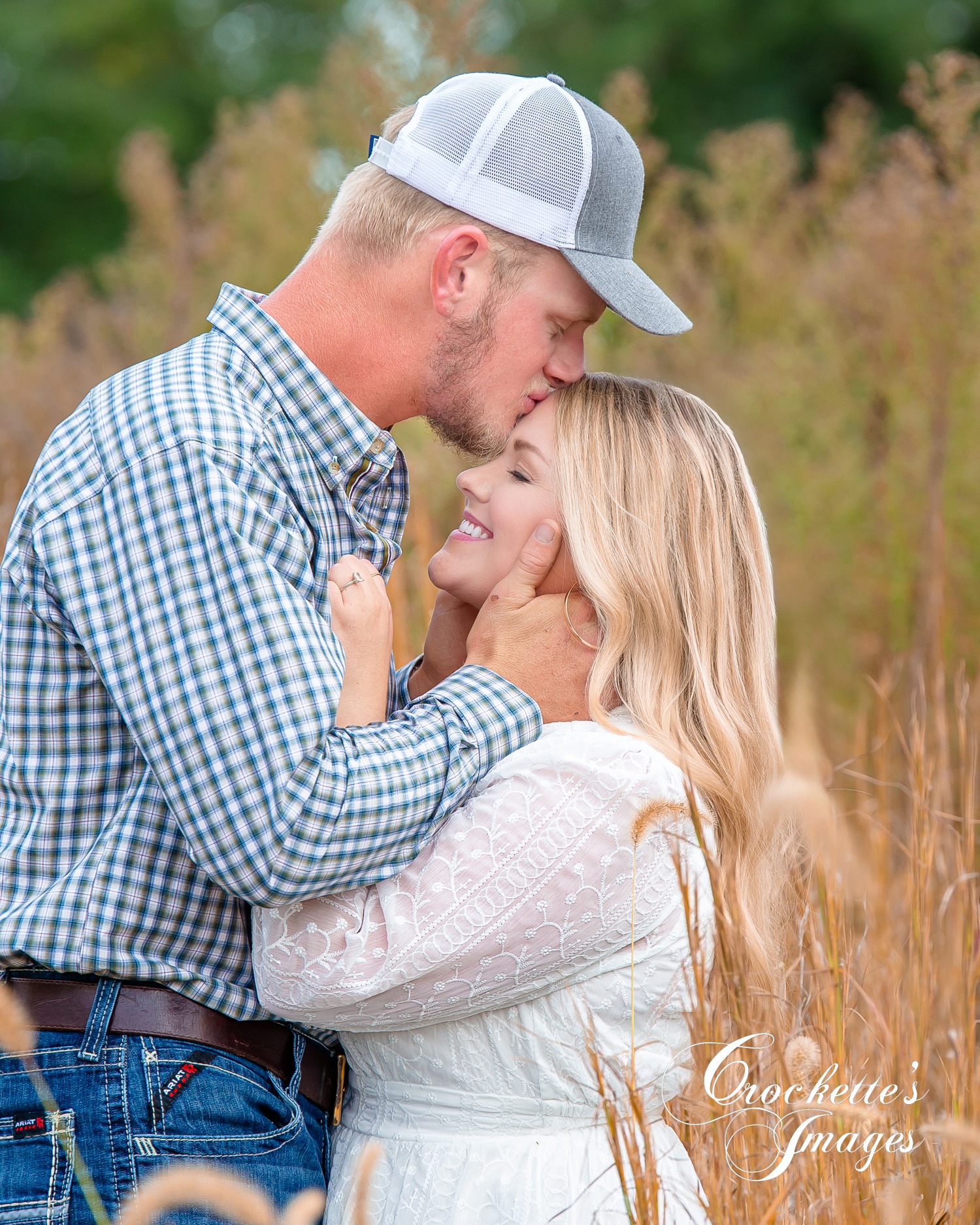 romantic fall engagement photo with man kissing girls forhead in a fall weedy field