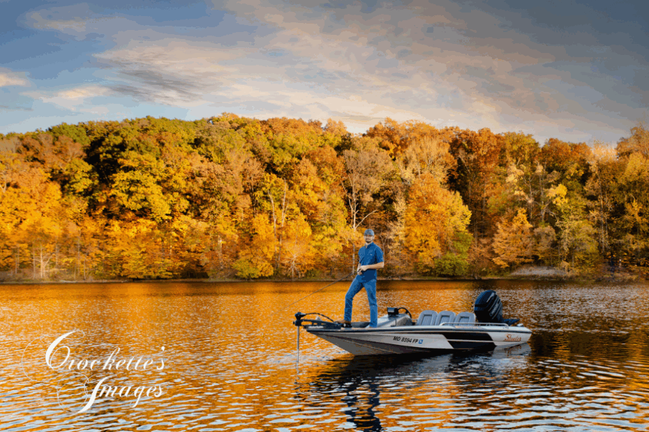 Senior boy fishing off a fishing boat in a pond with yellow and gold trees behind him.