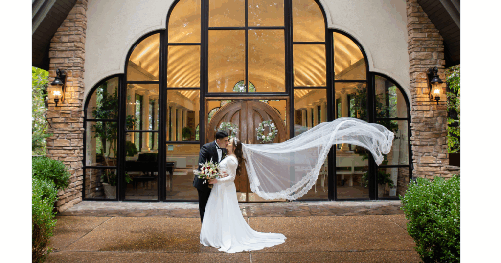 A classic flowing veil photo in front of the church with the groom kissing the bride. 