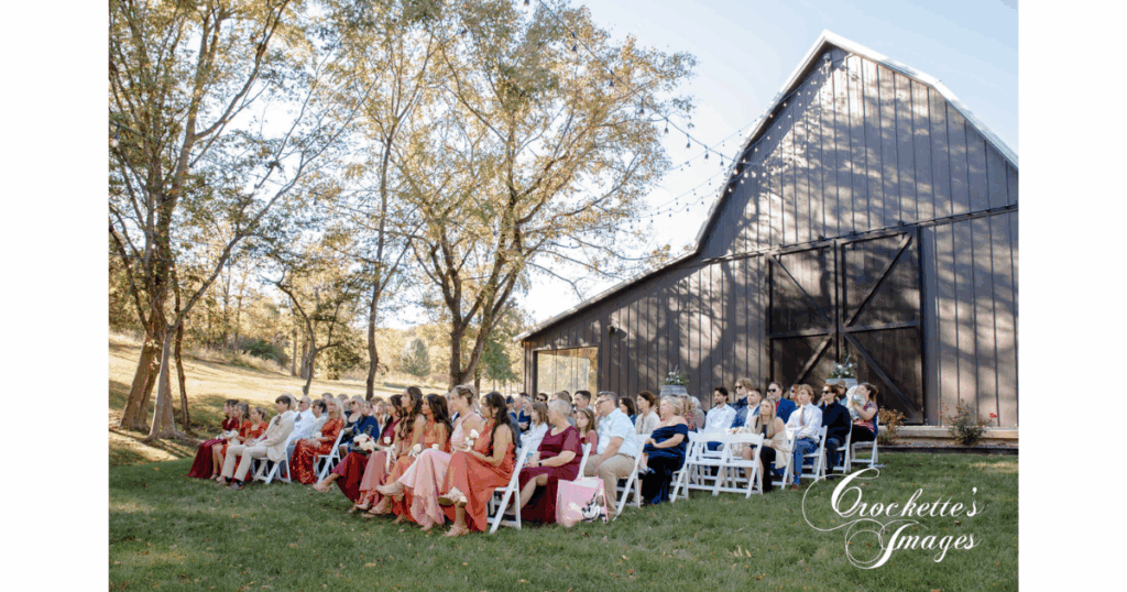 Wedding guests witnessing the union of a bride and groom during their outdoor wedding ceremony, with the venue in the background.