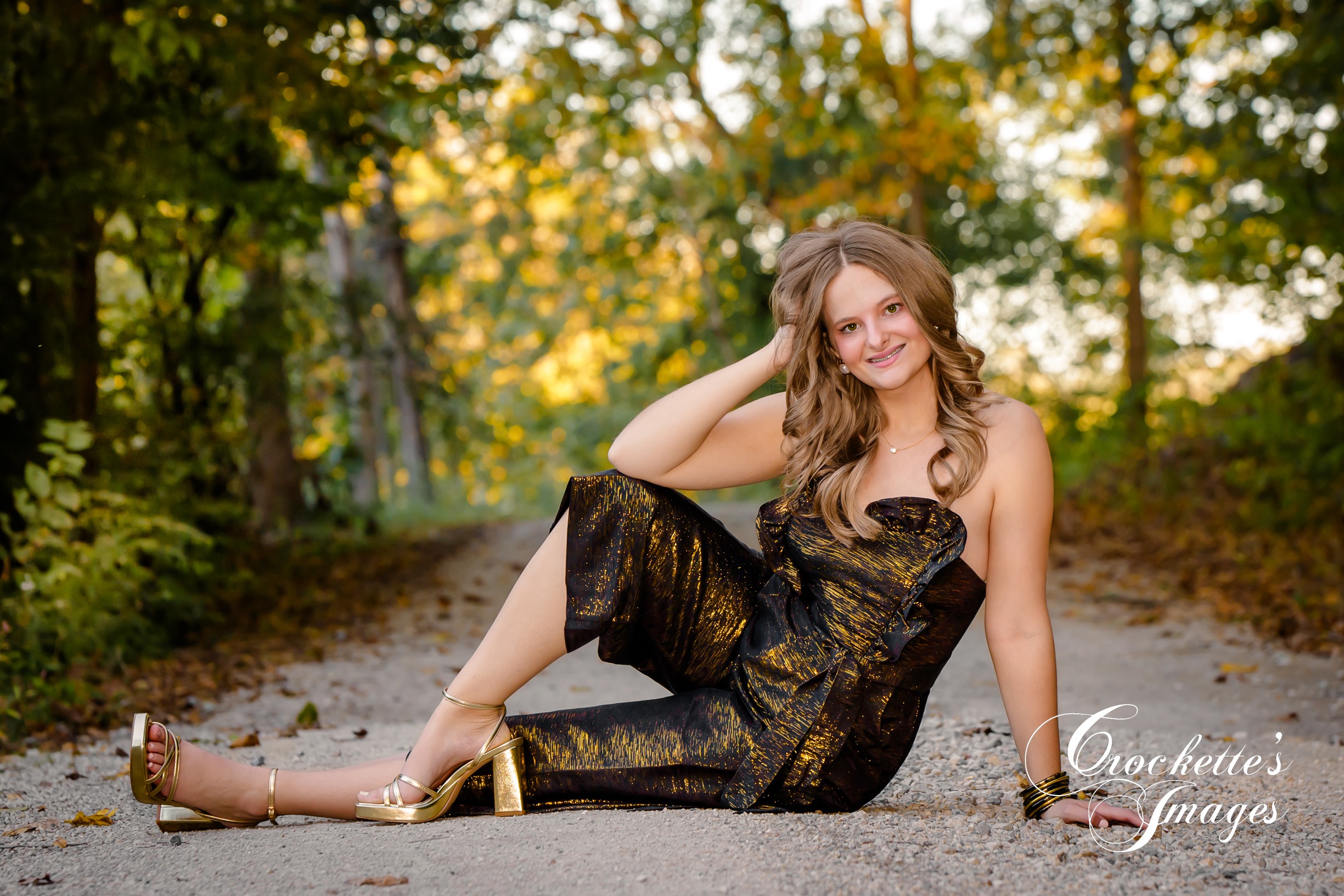 High School Senior Photo of a girl on a gravel road in a prom dress & gold heals surrounded by fall leaves
