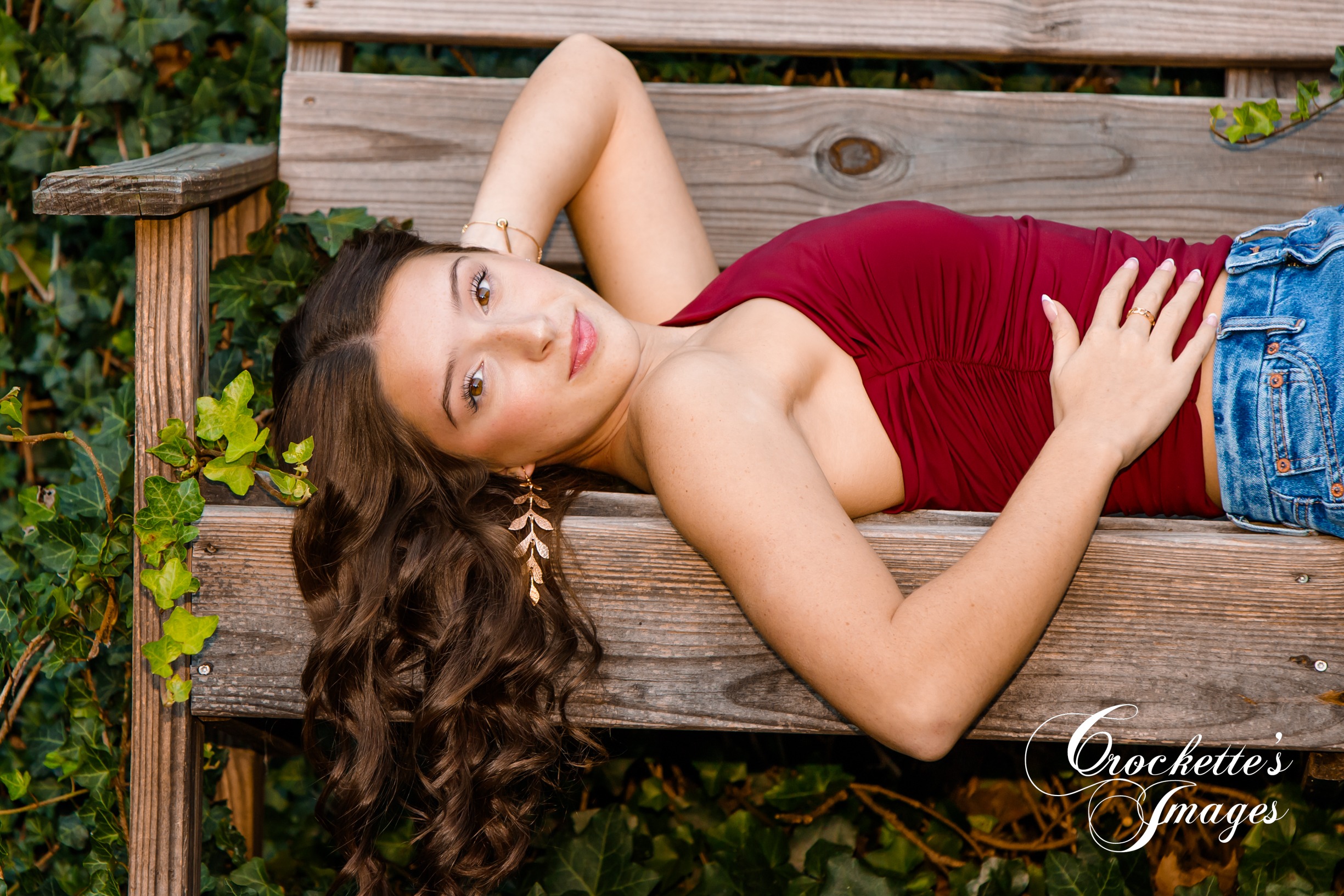 Senior photo of a HIgh School Senior Girl laying on a bench with green ivy and big gold earring