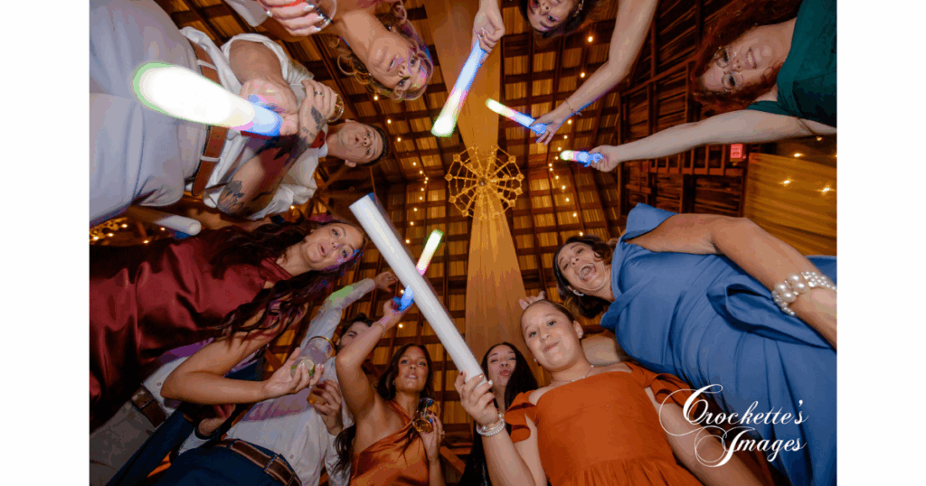 Wedding guests having fun at the reception as they are circled around the photographer, waving their party lights.