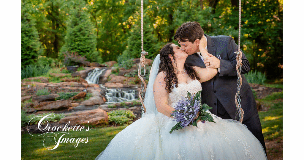 How to Pose With Your Bridal Bouquet for Timeless Wedding Photos You’ll Love Forever 4 Bride kissing groom while sitting on a swing with a gentle waterfall in the background during summer.