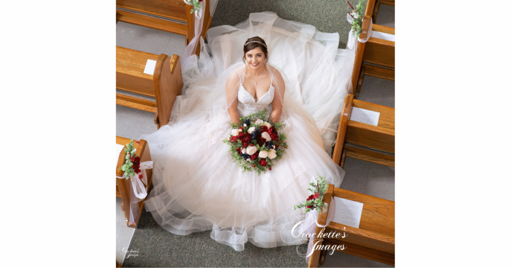 How to Pose With Your Bridal Bouquet for Timeless Wedding Photos You’ll Love Forever 3 Bride poses with her bouquet, seated in the aisle of the church as the photographer takes the image from above.