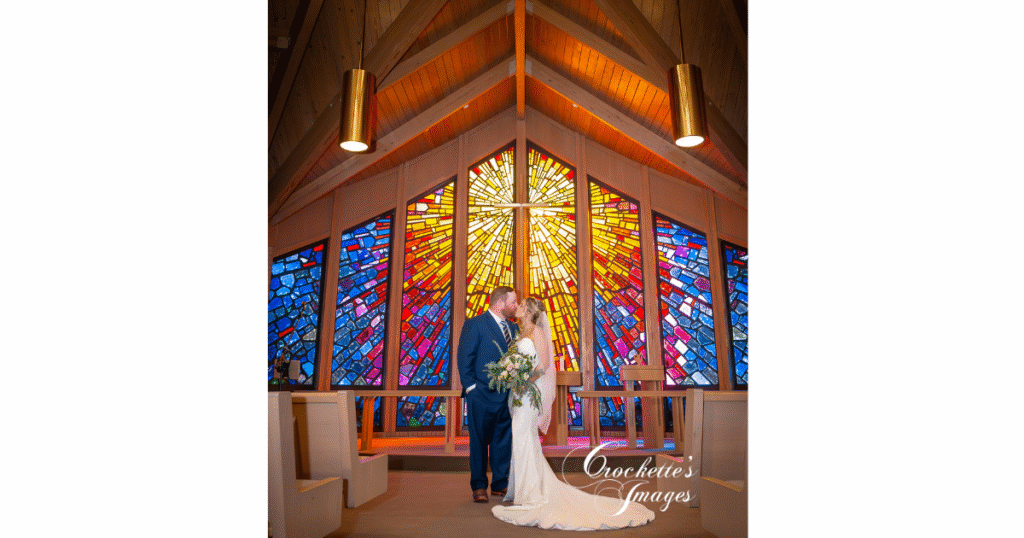 How to Pose With Your Bridal Bouquet for Timeless Wedding Photos You’ll Love Forever 5 Bride and groom pose in front of a beautiful stained glass window in a church.