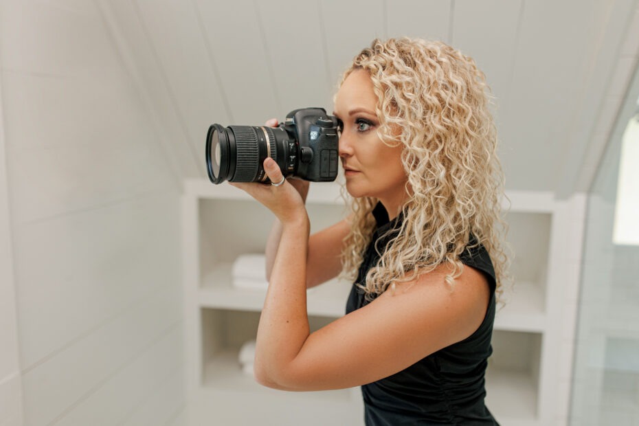 Wedding photographer taking photos indoors in a white-painted room, photographed from the side with no people visible in the background.