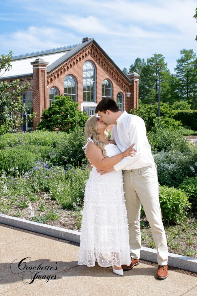A couple kissing in the garden in front of a building.