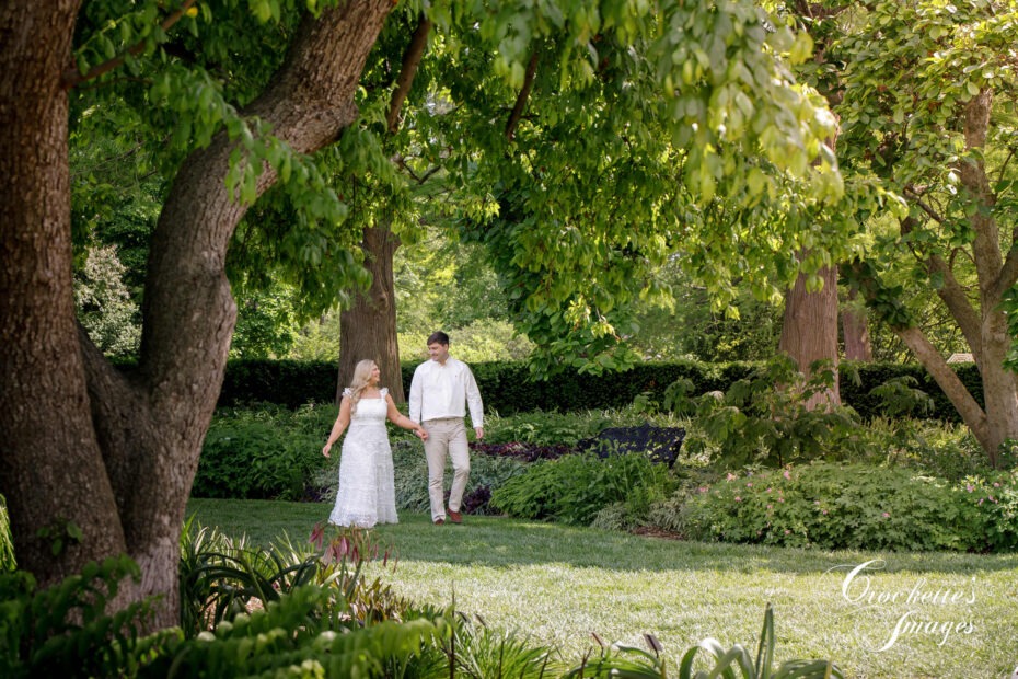 A happy couple walking through a garden holding hands.